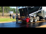 Dump truck driving backwards with body upright dispensing stone chips to Amerispreader shown at work dropping stone chips on a roadway in Quachita County Arkansas roadway